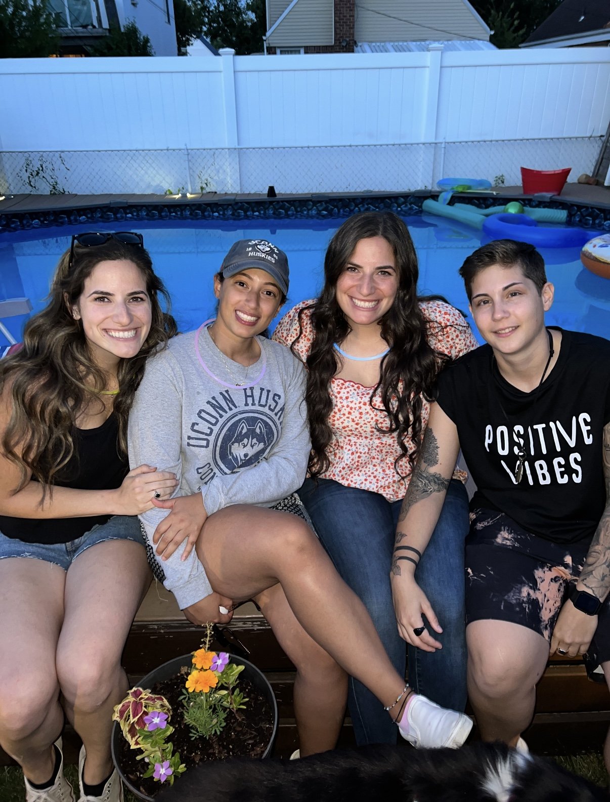 Four friends sitting by a backyard pool, one in a UConn Huskies sweatshirt